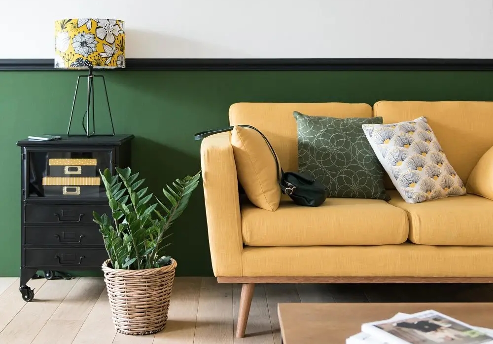 an ochre coloured soaf in front of a green wall with a coffee table and lamp on it