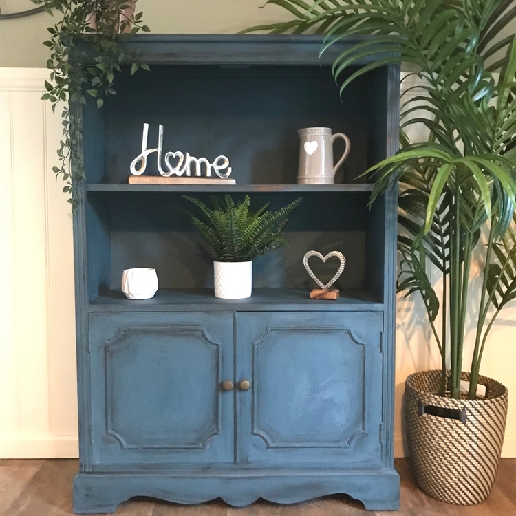 a blue painted dresser with vases and pots on the shelves with cupboard doors below and a plant by its side